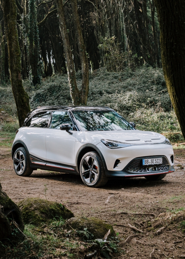 Ein weißer smart #1 BRABUS steht auf einer kleinen Lichtung im Wald. 