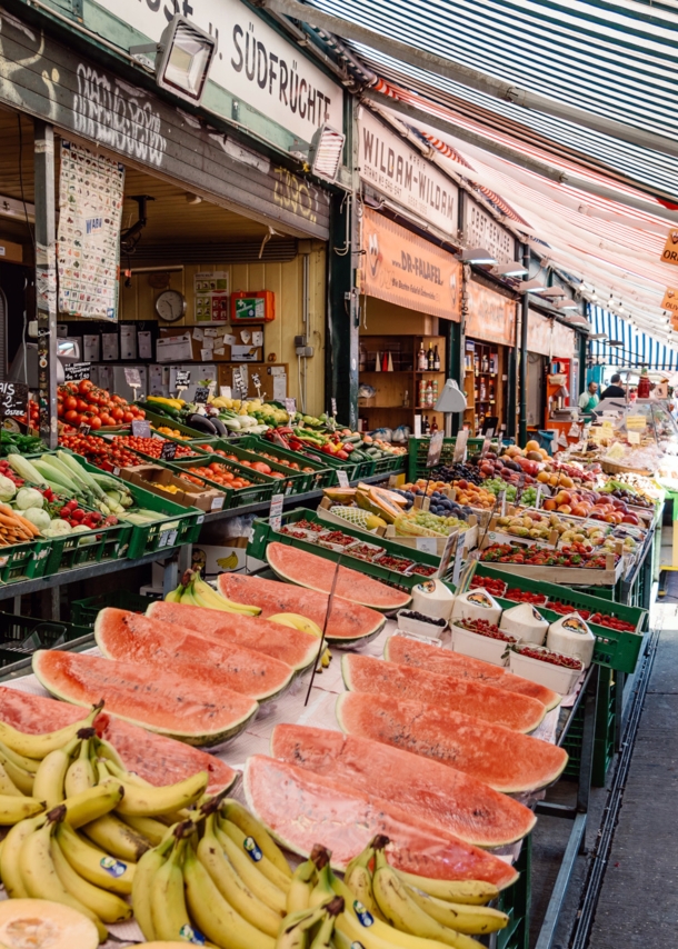 Personen auf einer Marktstraße mit Obst- und Gemüseauslagen.