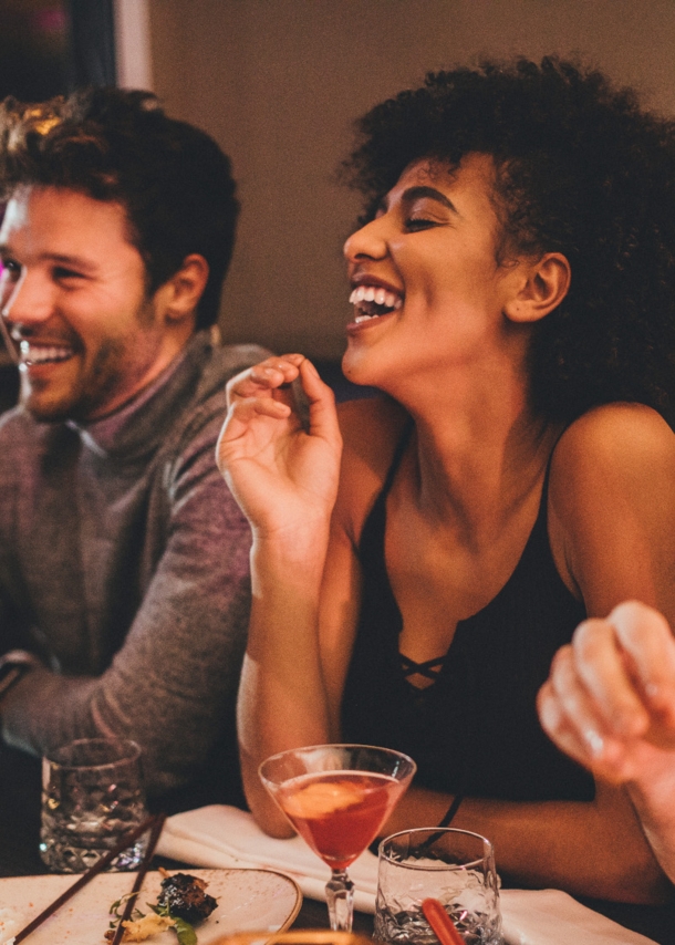 Eine Gruppe junger Menschen sitzt gut gelaunt mit Getränken an einem Tisch in einem Restaurant.