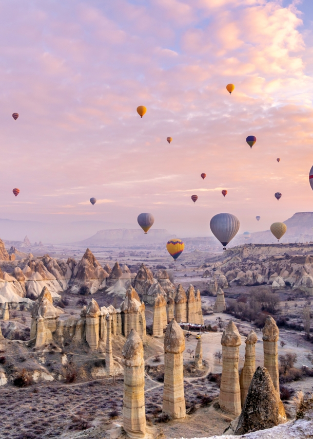 Heißluftballons über einer zerklüfteten Felslandschaft in Kappadokien bei Sonnenuntergang.