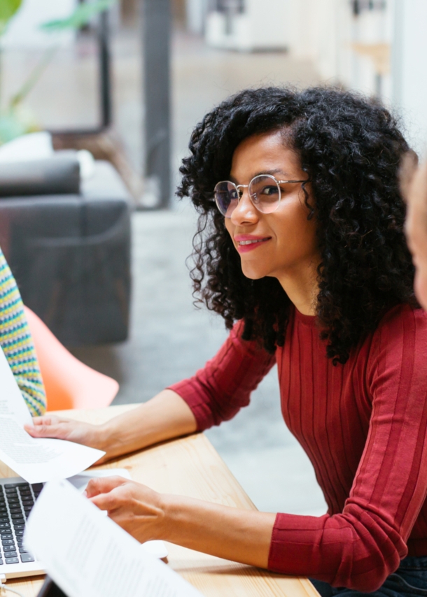 Drei junge Frauen sitzen mit Arbeitsunterlagen zusammen an einem Holztisch in einem Co-Working-Space.