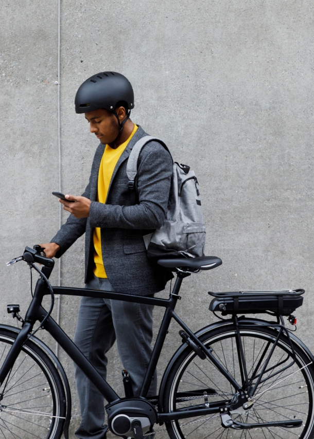 Ein junger Mann mit Rucksack und Fahrradhelm steht neben seinem E-Bike und schaut auf sein Smartphone.