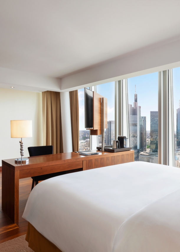 Modernes Hotelzimmer mit Blick auf die Frankfurter Skyline durch bodentiefe Panoramafenster.