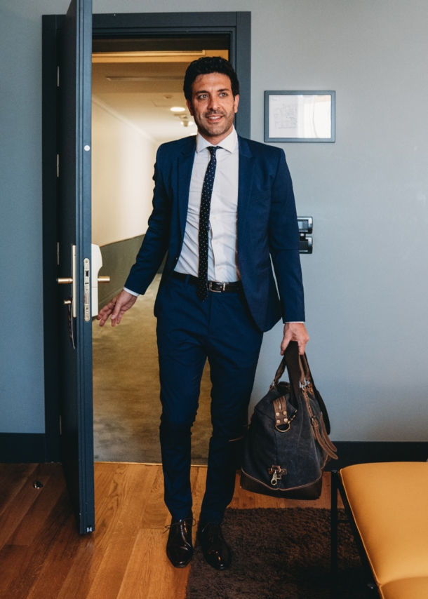 Ein Mann im Anzug trägt eine Reisetasche und betritt ein Hotelzimmer. 