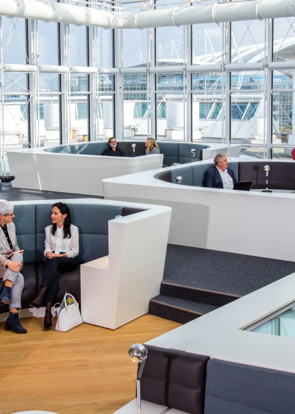 Mehrere Personen sitzen in einer modernen Sitzlandschaft einer Flughafenlounge mit Panoramafenstern.