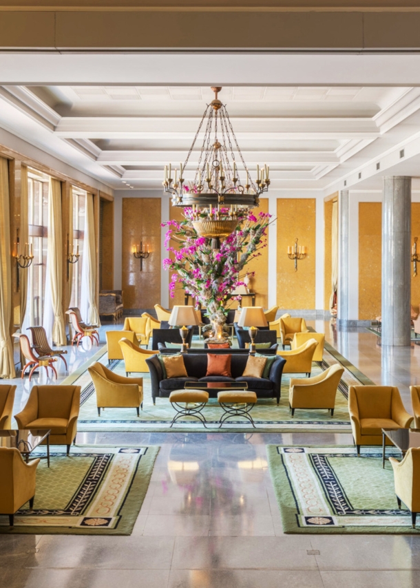 Ein elegantes Hotelfoyer mit Marmorsäulen und gelben Sesseln, in der Mitte ein großes Blumenbouquet.