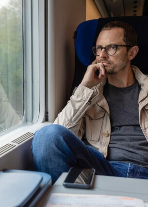 Mann sitzt in fahrendem Zug und schaut aus dem Fenster.