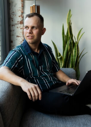 Benjamin Diedering sitzt mit Laptop auf dem Sofa und schaut aus dem Fenster