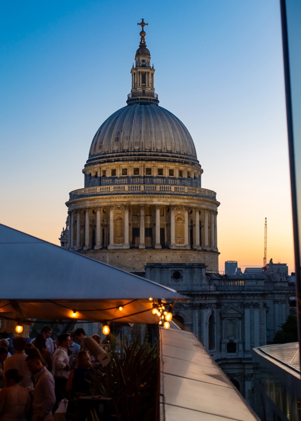 Belebtes Restaurant auf Dachterrasse vor der Kuppel der St Paul’s Kathedrale bei Abenddämmerung.