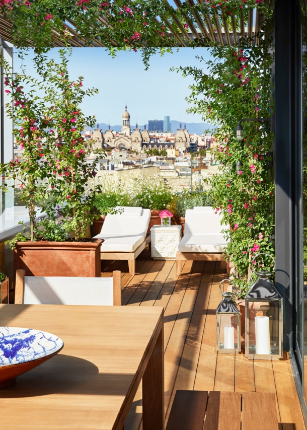 Hotelterrasse mit Liegen vor der Skyline Barcelonas bei Sonnenschein.