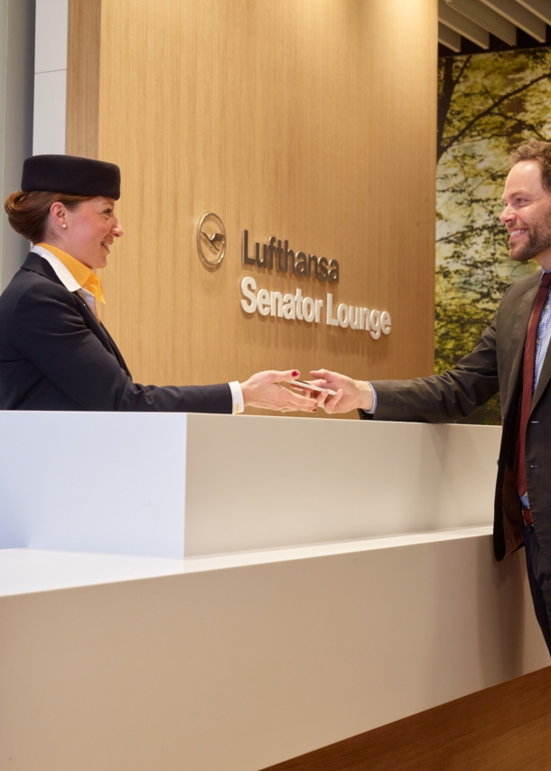 Eine Bodenstewardess begrüßt einen Gast beim Check-in am Empfang einer Lufthansa Senator Flughafenlounge.