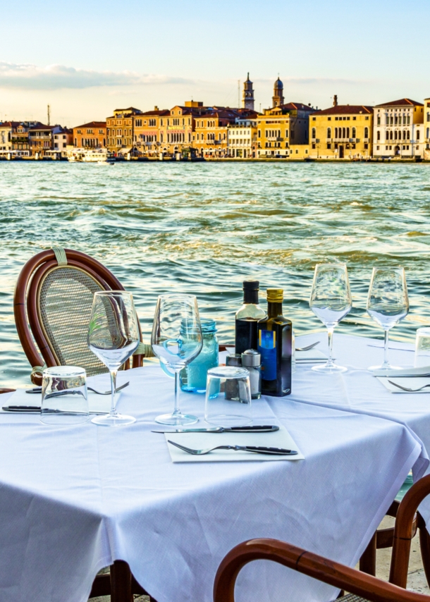 Ein gedeckter Tisch im Außenbereich eines Restaurants am Wasser in Venedig.