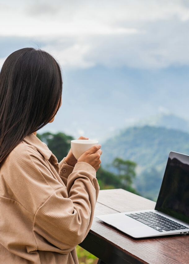 Junge Frau arbeitet auf dem Balkon am Laptop und genießt die Aussicht