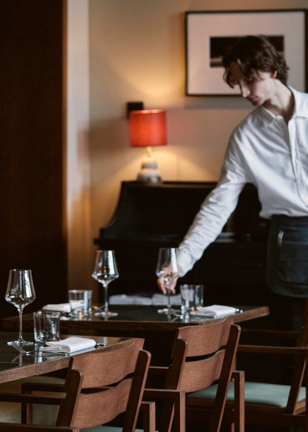 Ein junger Mann richtet ein Glas auf einem gedeckten Tisch in einem stilvollen Restaurant.