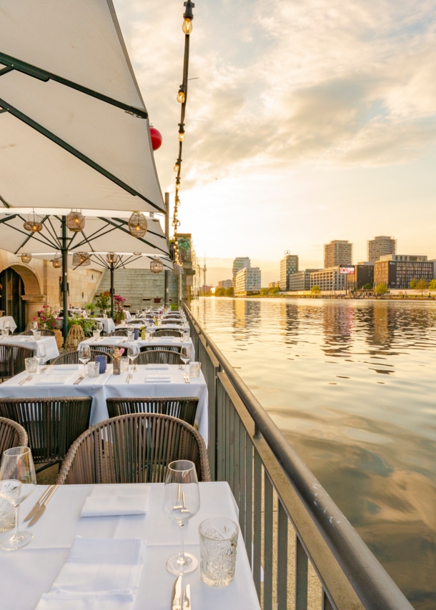 Weiß eingedeckte Tische auf der Terrasse eines eleganten Restaurants am Wasser in Berlin.