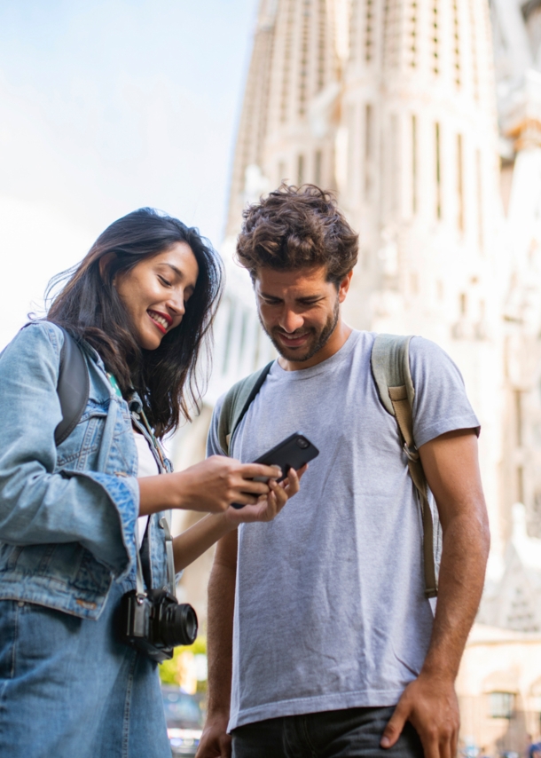 Zwei Personen stehen in Barcelona vor der Sagrada Família und blicken zusammen auf ein Smartphone.