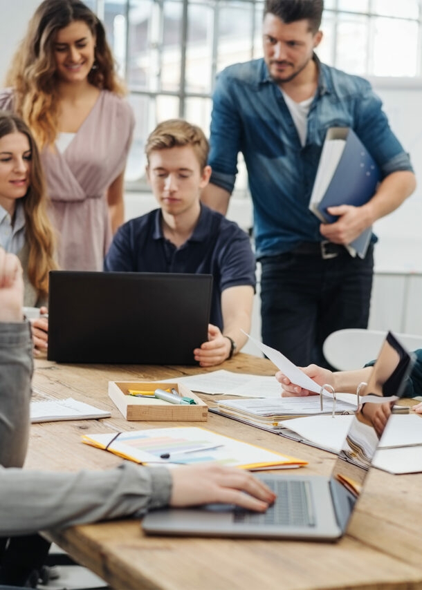 Mehrere Personen im hellen loftartigen Coworking-Space, stylishes Interieur, manche Personen konzentriert am Schreibtisch sitzend oder mit Laptop in einer Lounge-Zone, manche im Gespräch.