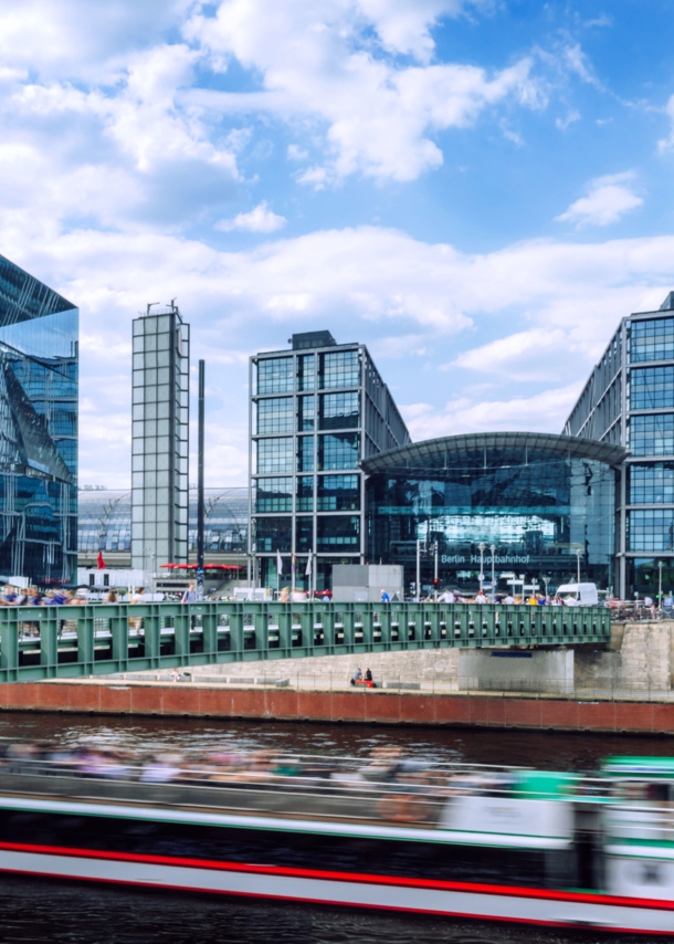 Modernes Bauensemble des Berliner Hauptbahnhofes mit Glasfassade am Flussufer, im Vordergrund ein Ausflugsboot in Unschärfe.