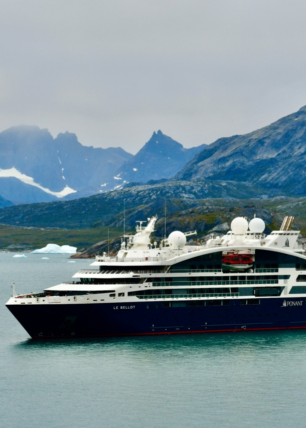 Das Bild zeigt im Vordergrund das Kreuzfahrtschiff. Im Hintergrund sind Berge und etwas Schnee und Eis zu sehen.