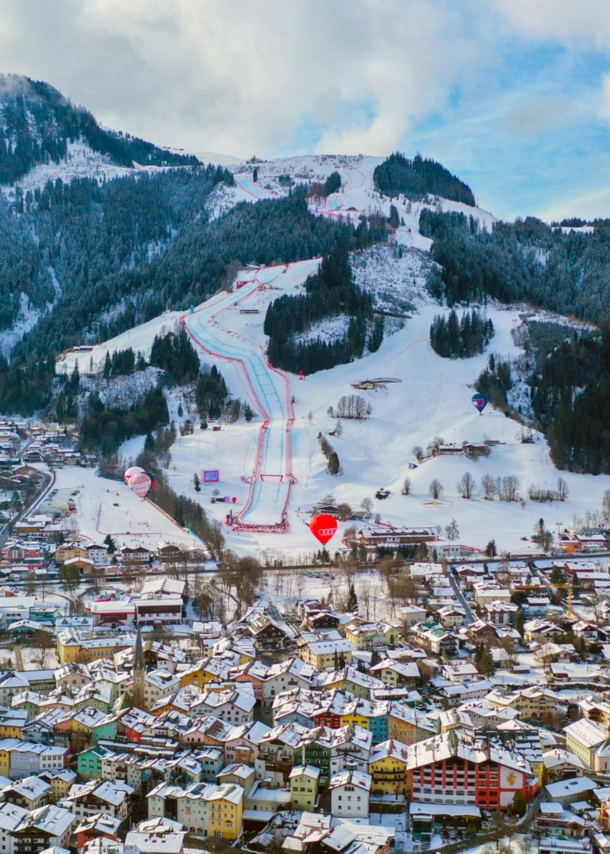 Schneebedecktes Stadtpanorama von Kitzbühel vor Berg mit Skipisten.