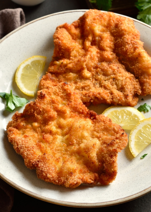 Ein Wiener Schnitzel auf einem Teller mit Zitronenscheiben.