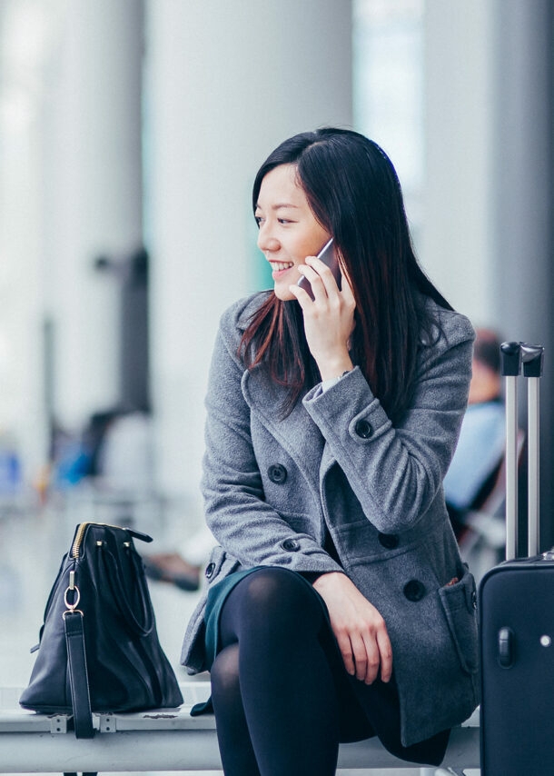 Eine asiatische Geschäftsfrau sitzt im Wartebereich eines Flughafens und telefoniert.