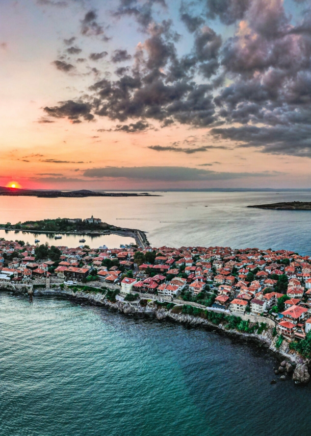 Ortschaft auf einer felsigen Landzunge im Meer unter Wolkenhimmel bei Sonnenuntergang.