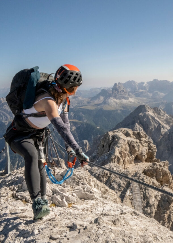 Eine Person mit Kletterausrüstung, die sich an einem Seil festhält, im Hintergrund Berge.