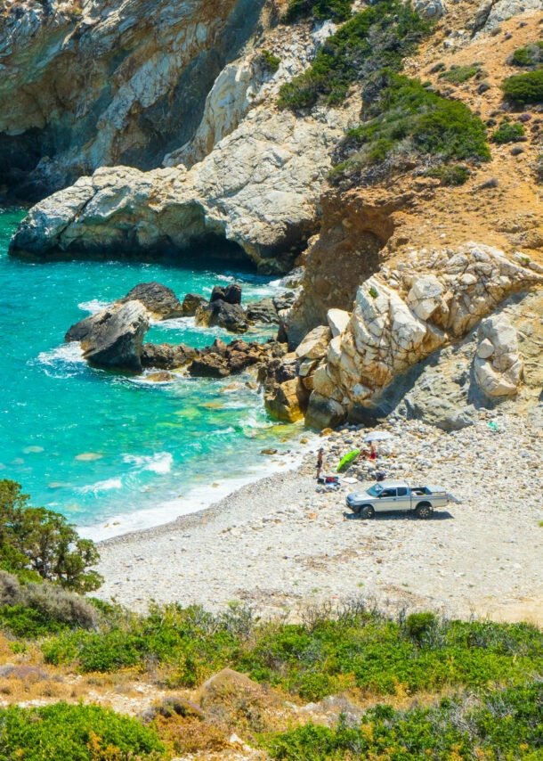 Ein Van steht auf einem Sandstrand in einer kleinen mediterranen Felsbucht mit türkisblauem Wasser.