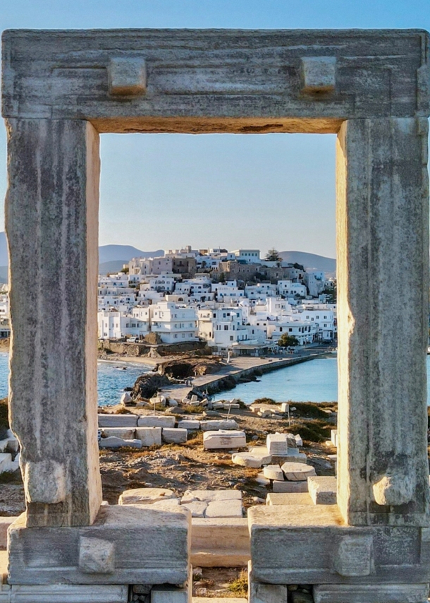 Blick auf die Stadt Naxos auf einer Insel durch ein Steintor in einer antiken Ruinenstätte auf einem Hügel.