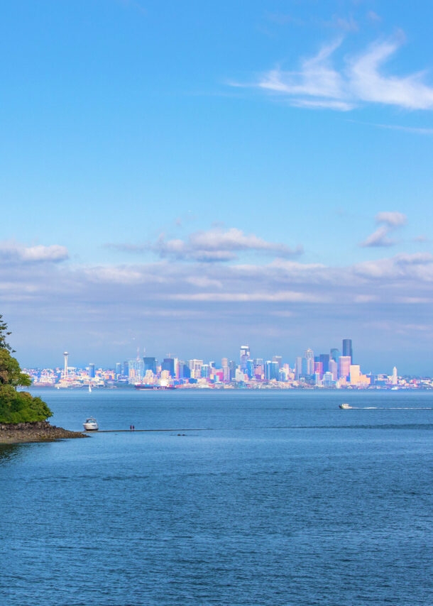 Vereinzelte Häuser auf einem schmalen Inselabschnitt, umgeben von Wasser vor Seattles Skyline im Hintergrund.