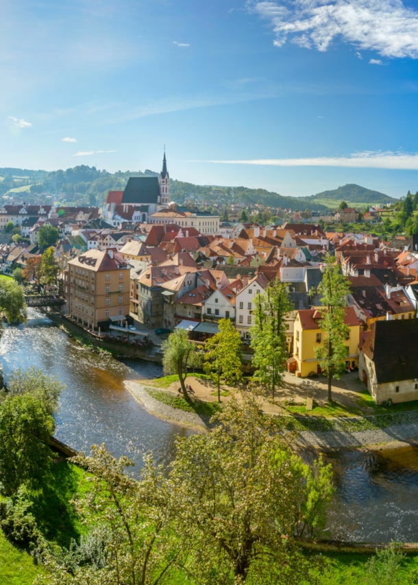 Mittelalterliche Kleinstadt mit Burg an einer Flussschlinge, umgeben von grünen Hügeln bei Sonnenschein.