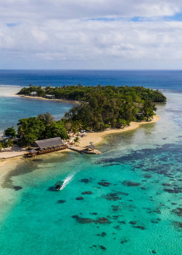 Kleine Insel mit Mangrovenwald und Bootsanleger an einem hellen Sandstrand, umgeben von türkisblauem Meer.