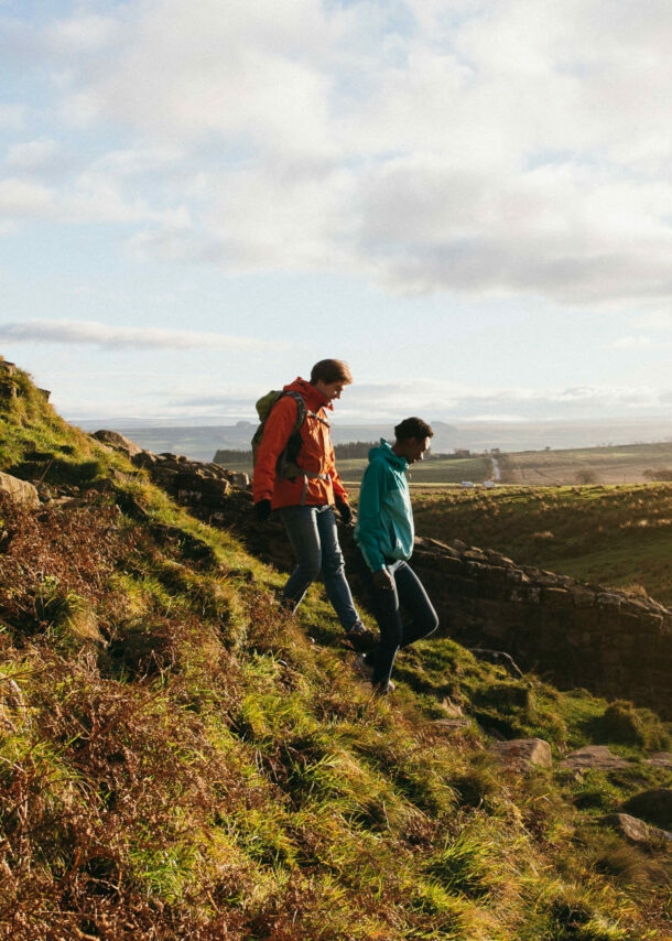 Zwei Personen laufen einen grünen Hügel am Hadrianswall hinab.