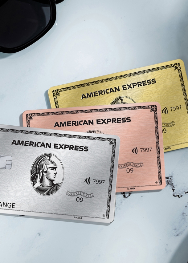 Drei Kreditkarten von American Express liegen auf einem Kaffeetisch aus Marmor, drum herum ist ein Croissants und eine Sonnenbrille.