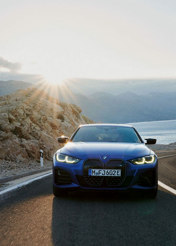 Vorderansicht eines blauen Autos der Marke BMW, das auf einer gebirgigen Küstenstraße fährt