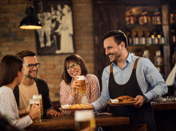 Lächelnder Kellner, der einer Gruppe von Gästen in einem Pub Essen bringt