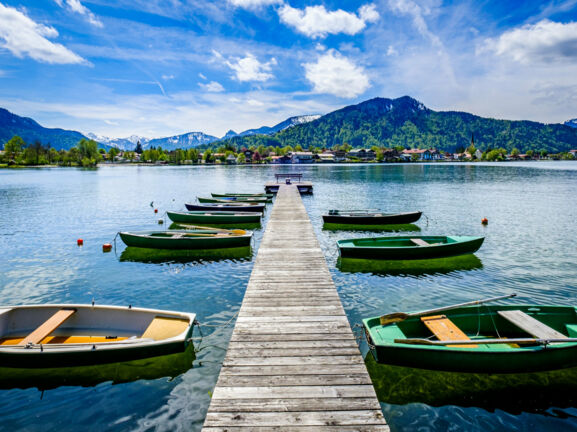 Ein Holzsteg mit kleinen Booten auf einem See, im Hintergrund Berge