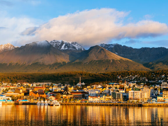 Stadtpanorama von Ushuaia am Wasser vor Bergkulisse im Sonnenuntergang