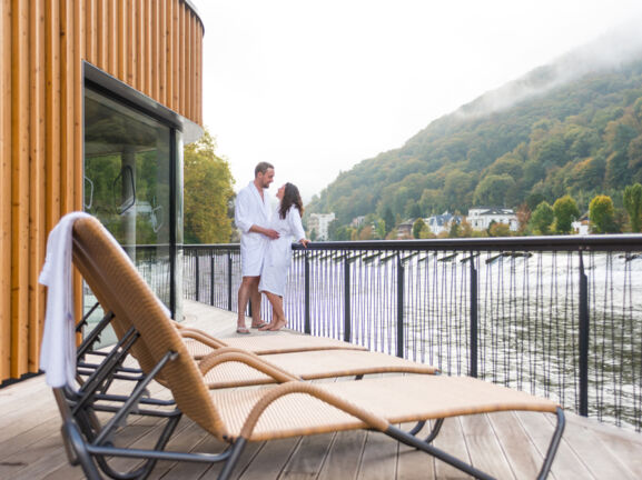 Ein Mann und eine Frau in weißen Bademänteln stehen auf dem Sonnendeck einer Flusssauna