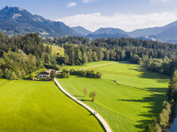 Blick auf eine Landschaft mit Bergen, Wiesen und einem Bach