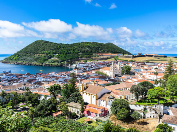 Mediterrane Kleinstadt am Meer, umgeben von grüner Hügellandschaft.