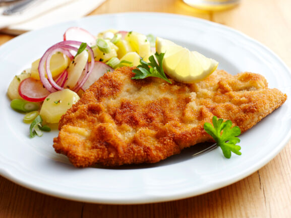 Ein paniertes Schnitzel mit Kartoffelsalat auf einem weißen Teller.