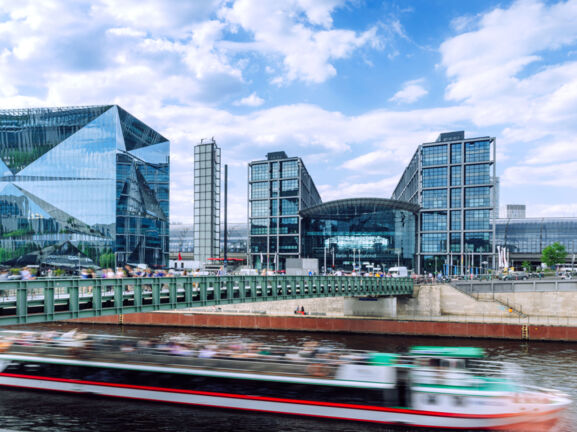 Modernes Bauensemble des Berliner Hauptbahnhofes mit Glasfassade am Flussufer, im Vordergrund ein Ausflugsboot in Unschärfe.