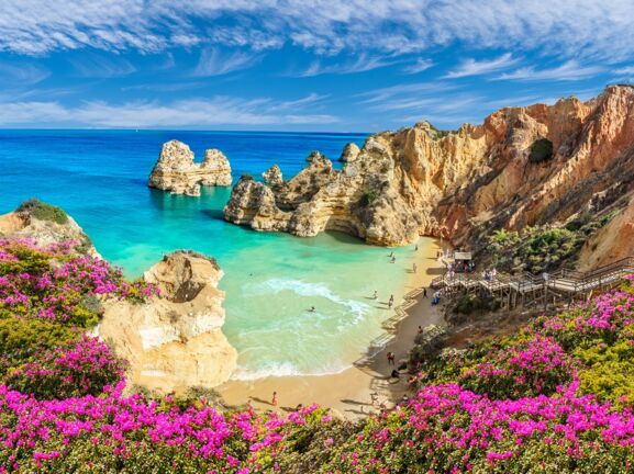 Blick von oben auf eine von Felsen umgebende Bucht und türkisblaues Meer an der Algarve.