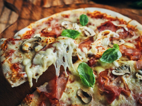 Nahaufnahme einer Pizza mit Champignons, Schinken und Basilikum auf zerlaufenem Käse.