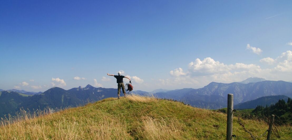 Mann schaut von einem Gipfel auf die umliegenden Berge