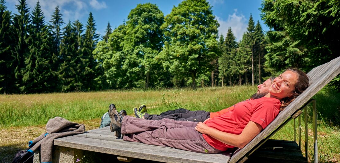 Ein Mann und eine Frau liegen auf Holzliegen und entspannen sich