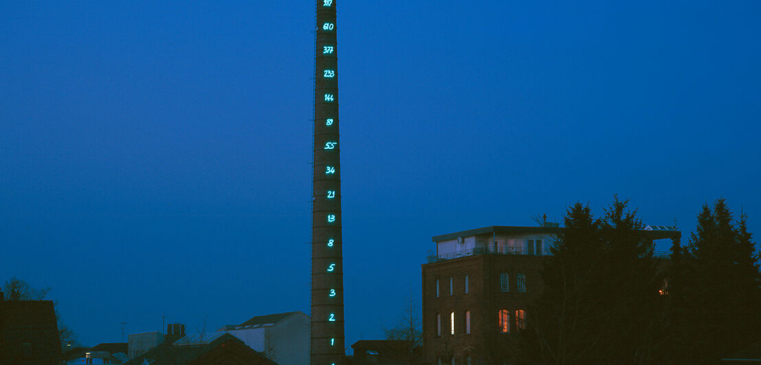 Ein Industrieschornstein mit einer leuchtenden Zahlenreihe