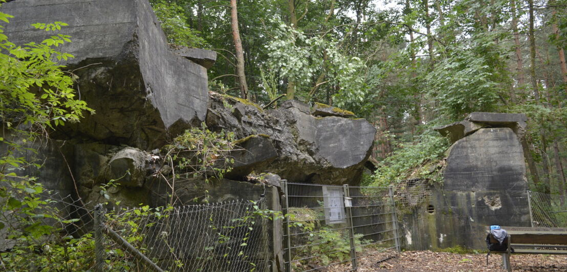 Hinter einem Zaun liegen massive und marode Steinplatten aufeinander